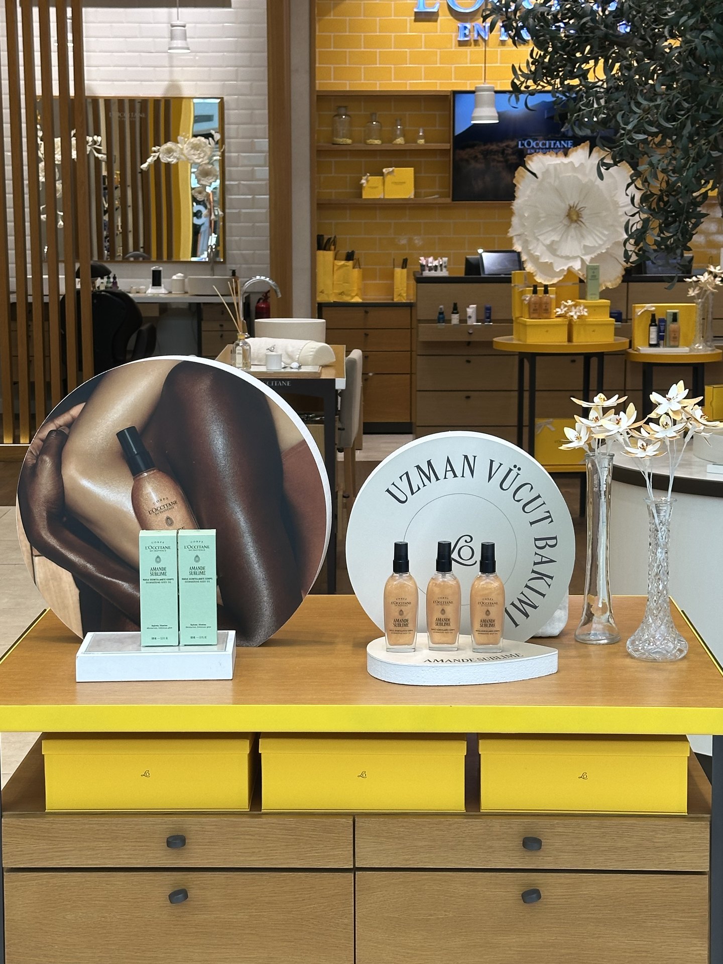 L'Occitane mağazasında strafor yuvarlak panolar, ürün sunum kaideleri ve dekoratif çiçekler
